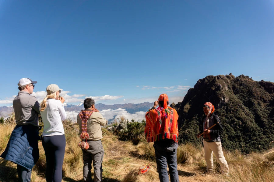 coca leaf ritual luxury family trekking peru Couple participating in a traditional coca leaf ritual with their guide during a luxury family trekking Peru experience, surrounded by mountains and misty clouds.